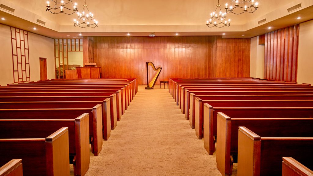A funeral service room at Sparkman/Hillcrest Funeral Home with cherry pews and a harp